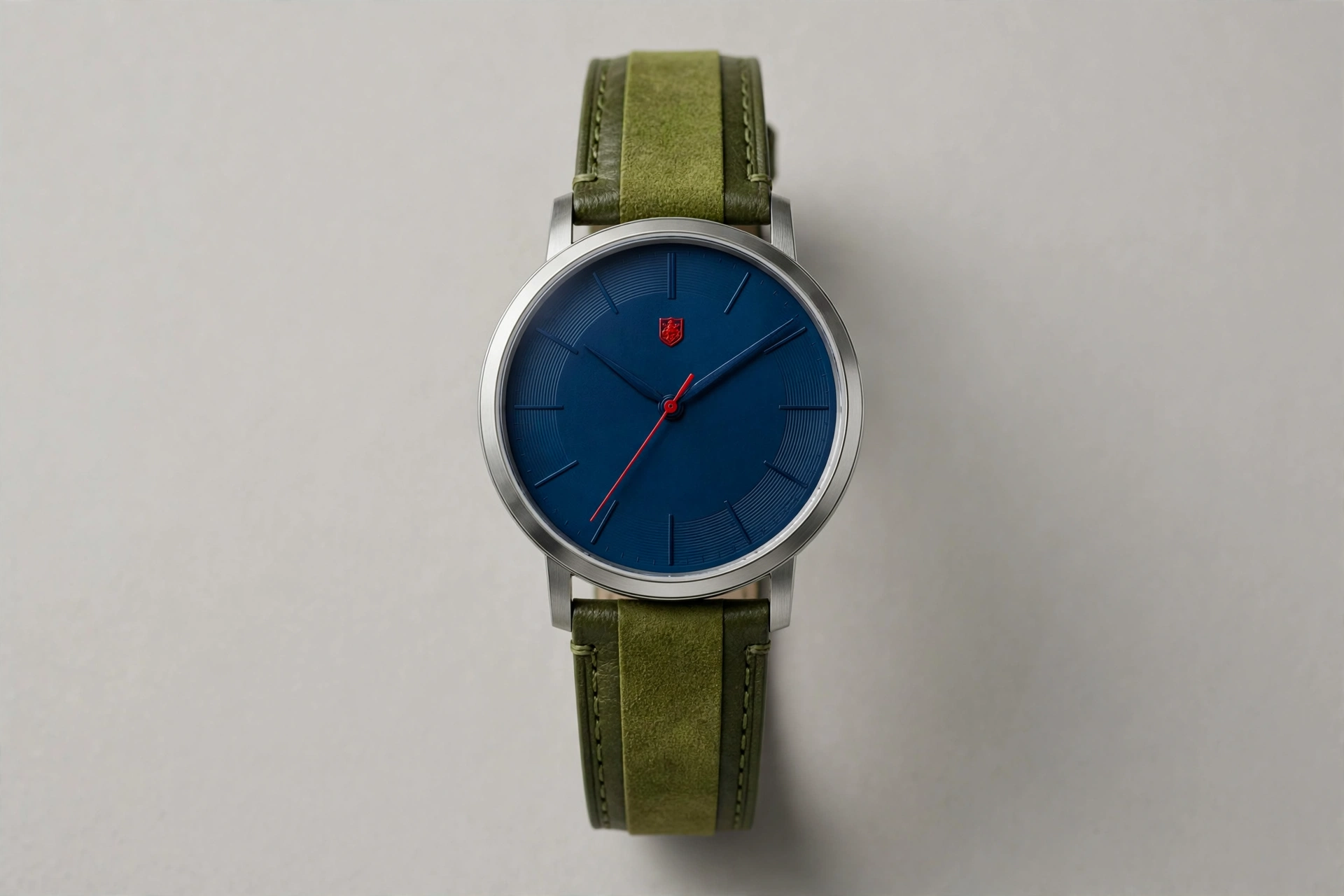 A watch with a navy dial and a two-tone olive strap, the red appearing only in the second hand and a small shield at twelve